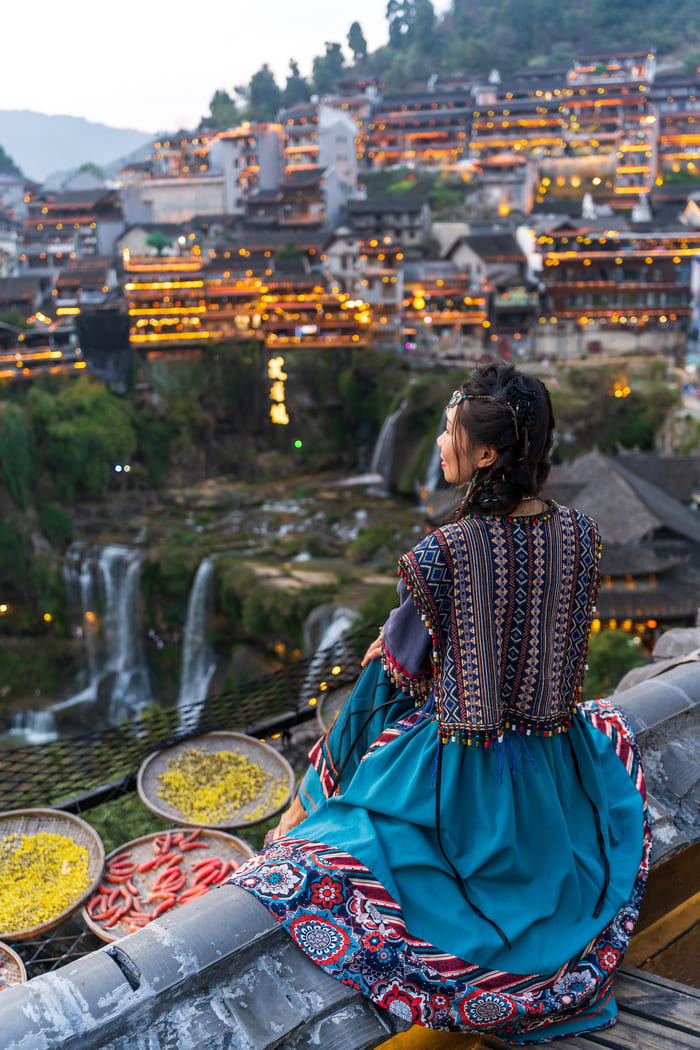 mujer con vestimenta tipica de la ciudad Lijiang China sentada contemplando la ciudad ,junto a unos platos con especies
